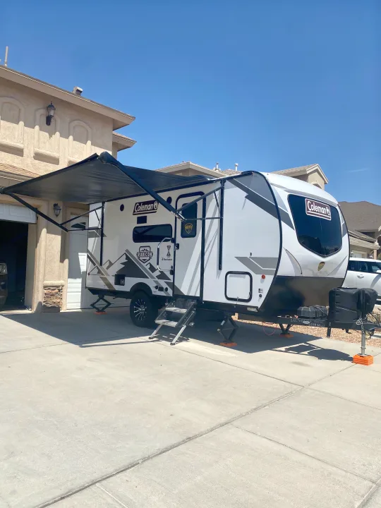 This white Coleman travel trailer RV rental, with awning deployed, sits ready on a sunny driveway, ideal for a memorable trip.. Dutchmen Coleman Rubicon 2022
