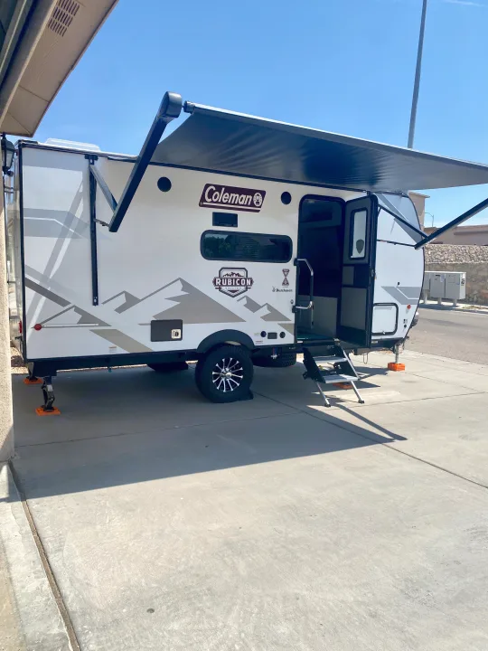 White Coleman Rubicon travel trailer RV rental, with awning extended and steps down, parked on concrete. Ready for outdoor adventure.. Dutchmen Coleman Rubicon 2022