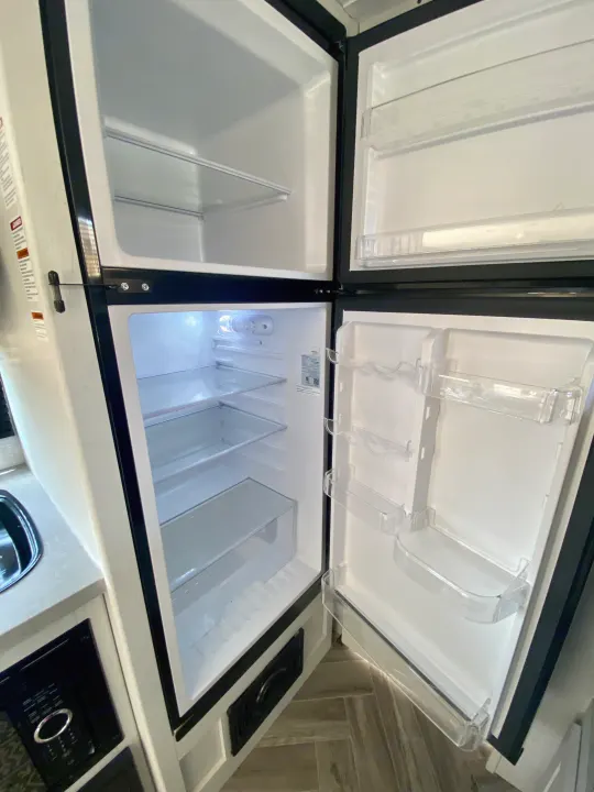An open, clean RV rental refrigerator and freezer, featuring multiple shelves and door storage.. Dutchmen Coleman Rubicon 2022