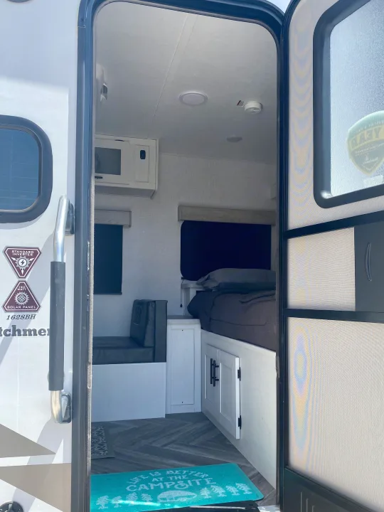 RV rental interior from the entrance. Features a dinette, bed, microwave, and a 'Campsite' mat. Ready for adventure.. Dutchmen Coleman Rubicon 2022