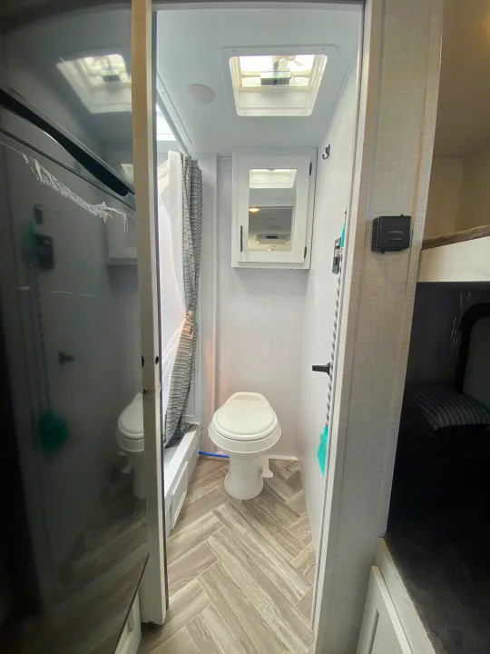 Compact **rv rental** bathroom: toilet, shower with curtain, mirrored cabinet, ceiling vent, and herringbone flooring.. Dutchmen Coleman Rubicon 2022