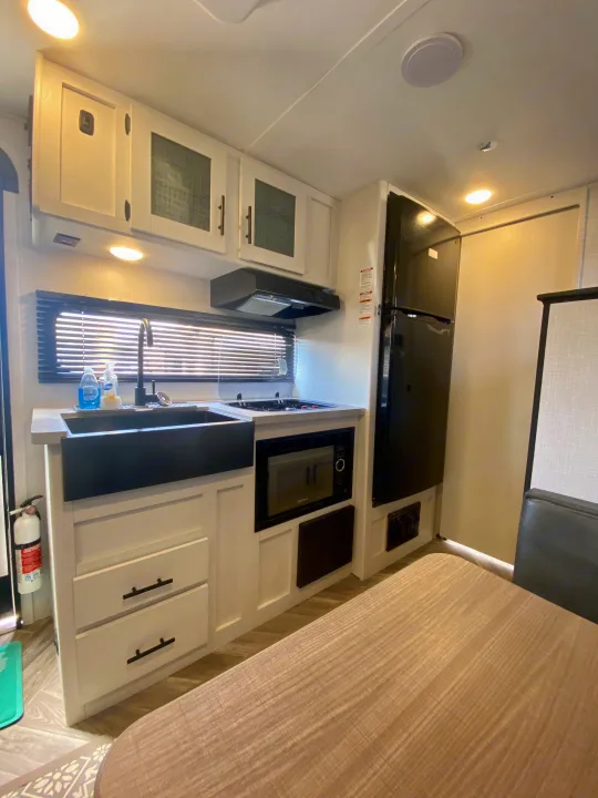 Bright, modern RV kitchen for your rv rental escape. Features white cabinets, black sink, stove, microwave, and fridge.. Dutchmen Coleman Rubicon 2022