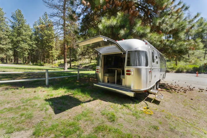 Airstream rv rental, hatch open, at a sunny, tree-lined campsite. Enjoy outdoor travel & nature.. Airstream Flying Cloud 2023