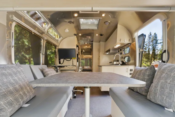 Step inside this modern RV rental! A comfy Airstream interior with dining, kitchen, and scenic forest views for travel.. Airstream Flying Cloud 2023