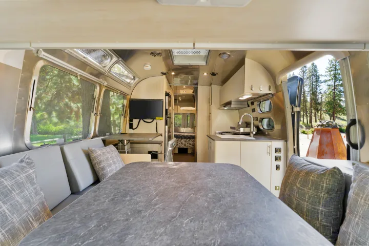 A stylish RV rental interior, showcasing a modern kitchen, dining area, and rear bedroom. Large windows reveal trees.. Airstream Flying Cloud 2023