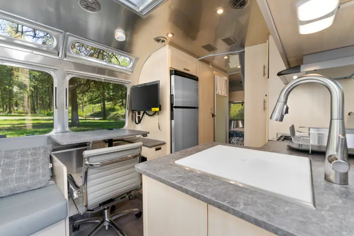 Functional RV rental interior: kitchen, desk, and large windows with serene forest views. Perfect for your next adventure or remote work.. Airstream Flying Cloud 2023