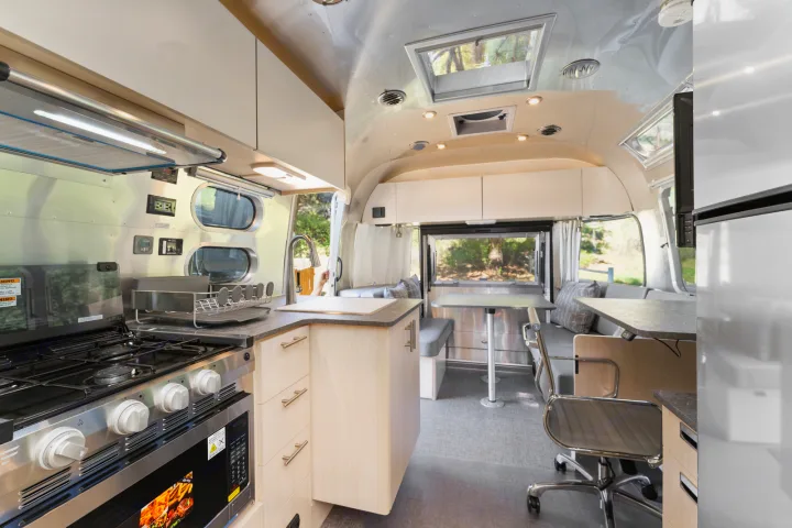 Spacious RV rental interior featuring a modern kitchen, dining area, and workspace, perfect for adventurous travel.. Airstream Flying Cloud 2023