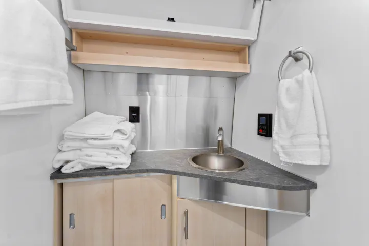 Step into comfort: This RV rental's compact bathroom/kitchenette features a sink, wood cabinets, stainless steel details, and fresh towels.. Airstream Flying Cloud 2023