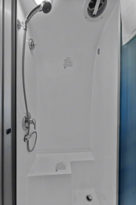 Compact, modern shower inside an RV rental, featuring a hand-held head, mixing valves, and built-in seat.. Airstream Flying Cloud 2023