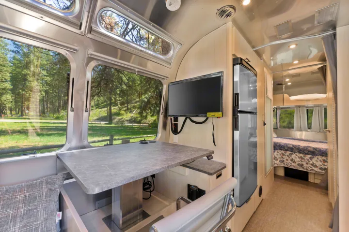 Explore this modern Airstream RV rental. Features large windows, a desk, TV, fridge, and a private bedroom area.. Airstream Flying Cloud 2023
