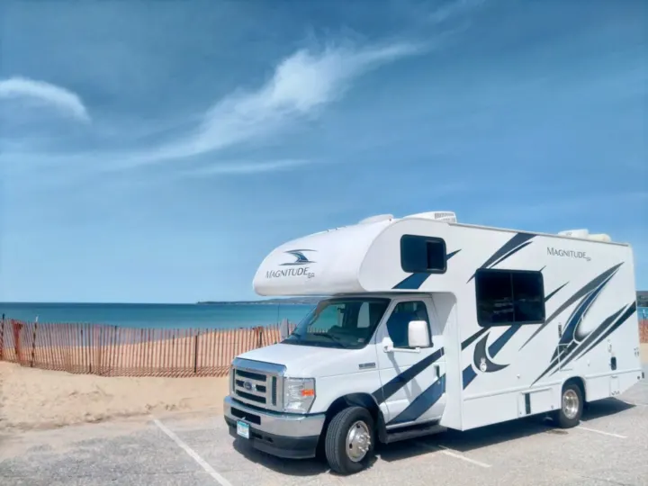 White Magnitude RV rental parked at a beachside lot with sand, ocean, and blue sky.. Thor Magnitude 2021