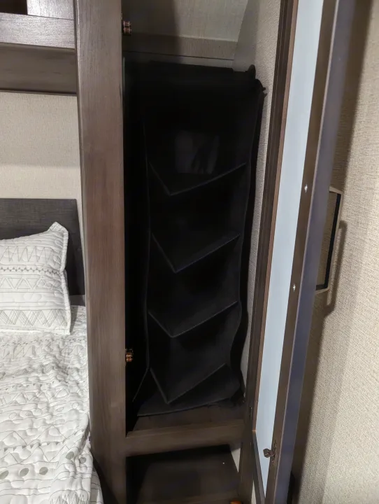 Efficient RV rental storage: a compact wardrobe features a hanging organizer with shelves and a full-length mirrored door.. Grand Design Transcend Xplor 2022