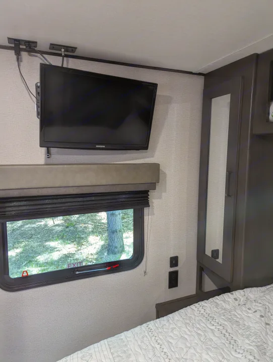 RV rental bedroom view: wall-mounted Samsung TV, window with blinds, and USB outlets beside a bed and wardrobe.. Grand Design Transcend Xplor 2022