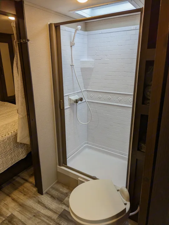 RV rental bathroom: compact shower with clear door, white tiles, and toilet. Ideal for travel.. Grand Design Transcend Xplor 2022