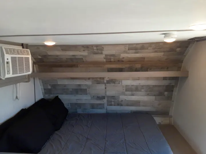 Cozy RV rental bedroom with a large bed, distressed wood accent wall, and a convenient air conditioner unit.. Coleman Other 2022