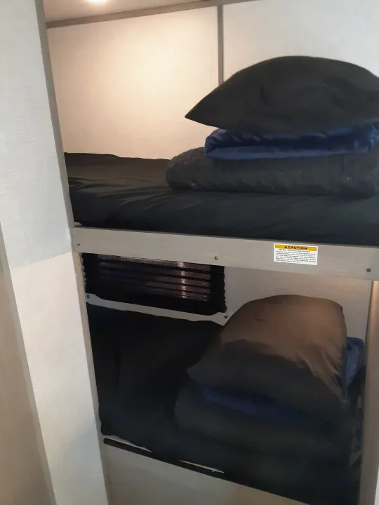 RV rental bunk beds with dark bedding and a 300 lbs. maximum capacity safety sticker, providing compact sleeping.. Coleman Other 2022