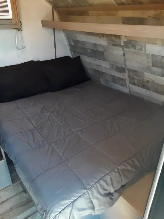 RV rental bedroom: a cozy, compact space with a grey quilted bed, black pillow, and angled wood plank ceiling.. Coleman Other 2022