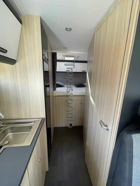 This RV rental interior shows a narrow hallway leading to a cozy bedroom, featuring a compact sink area and light wood cabinetry.. SunLiving A 75 DP 2024