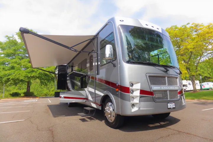 This spacious, grey motorhome with an extended awning and open compartments is parked, ready for your next RV rental.. Coachmen Encore 2024