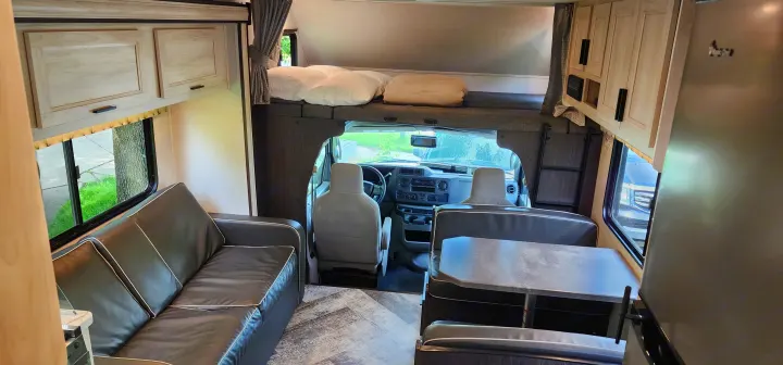 Inside a clean RV rental: living area with sofa, dinette, and overhead bunk above driver's cab. Ready for adventure!. Forest River Sunseeker LE 2021