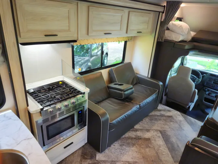 RV rental interior: kitchen with stove and microwave, spacious sofa, and overhead bunk for adventurers.. Forest River Sunseeker LE 2021