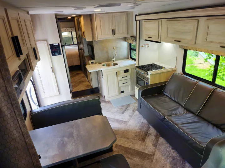 Modern RV rental interior featuring a full kitchen, dining area, comfortable sofa, and hallway to the bedroom, ideal for travel.. Forest River Sunseeker LE 2021