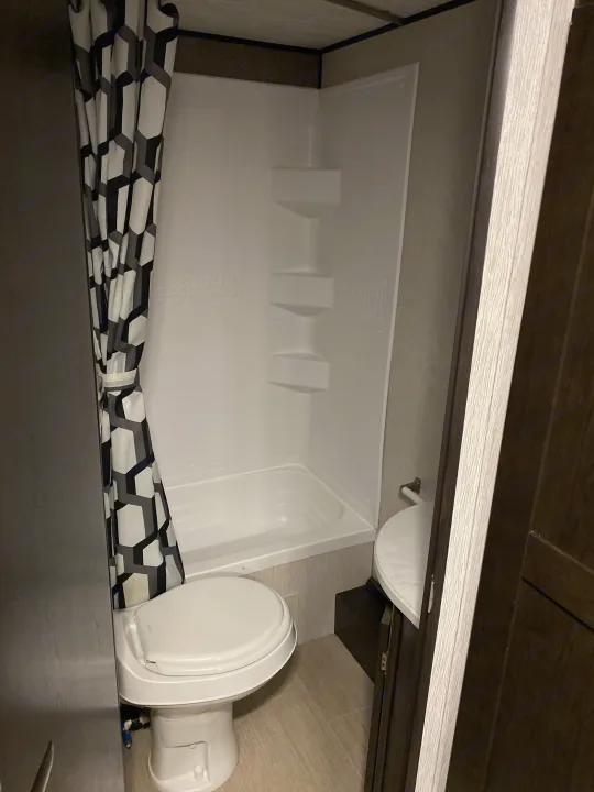 Compact RV rental bathroom with shower/tub combo, toilet, and vanity sink. Geometric shower curtain visible.. Heartland RVs Prowler 2021