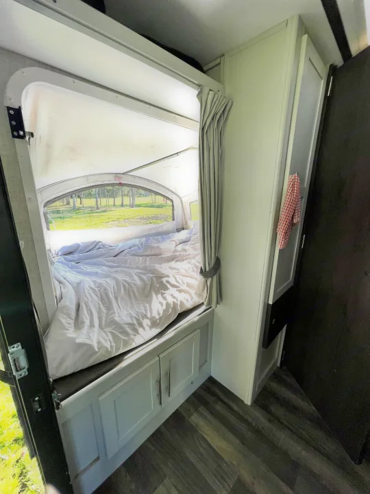 This RV rental shows a cozy bedroom with a large window offering a scenic view of trees and grass. Features a bed with white bedding and storage cabinets.. Keystone RV Bullet Crossfire 2019