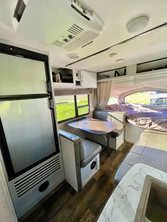 Interior of an RV rental: Compact living space with a dinette, refrigerator, and a pop-out bed area. Ideal for travel.. Keystone RV Bullet Crossfire 2019