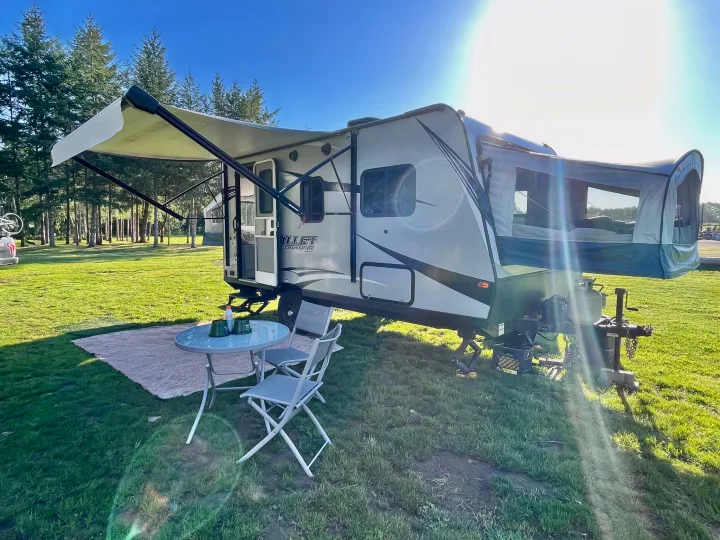 Spacious RV rental, a travel trailer with an extended awning, table, & chairs at a sunny campsite. Perfect for outdoor living.. Keystone RV Bullet Crossfire 2019