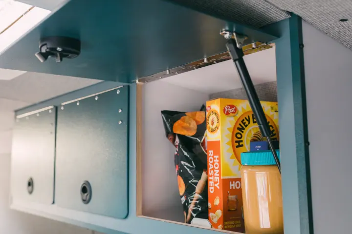 Open overhead cabinet in an RV rental, stocked with Honey Bunches of Oats cereal, chips, and peanut butter for road trip snacks.. Ford Transit 250 RWD 2018