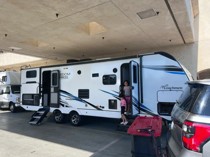 White Coachmen RV rental travel trailer with kids on steps, ready for family adventures.. Coachmen freedom express 287bhds 2022