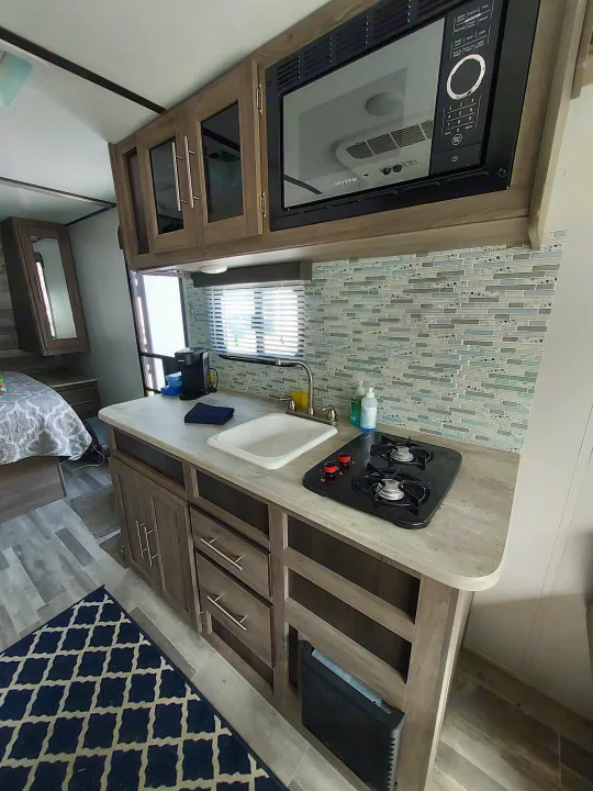 This RV rental features a compact kitchenette with microwave, sink, two-burner stove, stylish backsplash, and ample cabinetry.. Crossroads RV Zinger Lite 2022