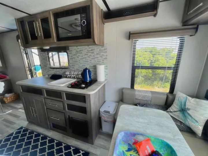 Compact RV rental kitchen and dinette, featuring a microwave, sink, stove, and comfortable seating with a scenic view.. Crossroads RV Zinger Lite 2022