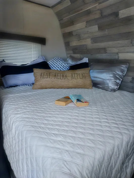 Cozy RV rental bedroom featuring a quilted bed, themed pillows, books, and rustic wood-paneled walls.. Crossroads RV Zinger Lite 2022