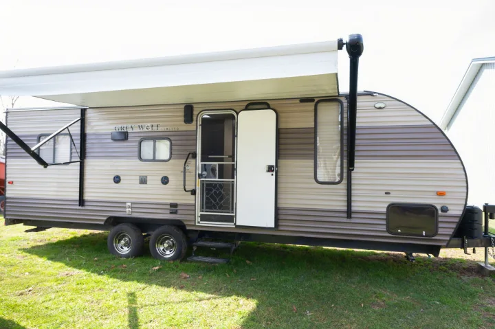 Tan Grey Wolf travel trailer for rv rental, with an extended awning & open screen door.. Forest River Cherokee Grey Wolf 2018