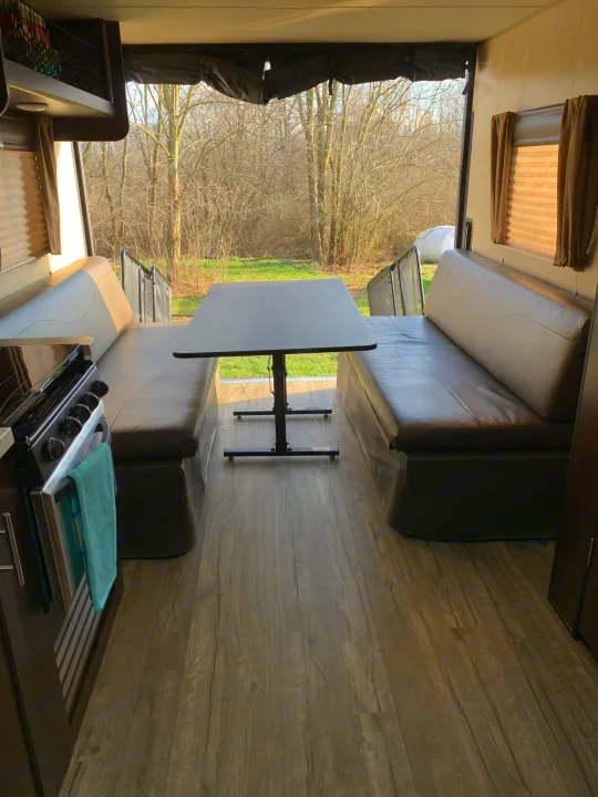 Bright RV rental interior with a cozy dining area: two brown benches, a table, and a lovely outdoor view, all on wood-look flooring.. Forest River Cherokee Grey Wolf 2018