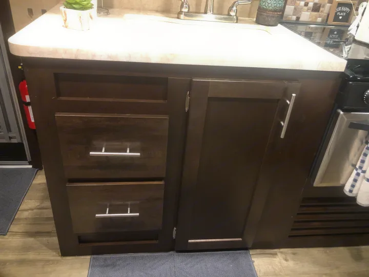 RV rental kitchen featuring dark cabinets, two drawers, a sink, and a stovetop. Fire extinguisher mounted on the side.. Forest River Cherokee Grey Wolf 2018