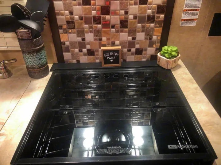 An RV rental kitchen features a clean, covered Suburban cooktop, decorative tile backsplash, and utensils in a holder.. Forest River Cherokee Grey Wolf 2018