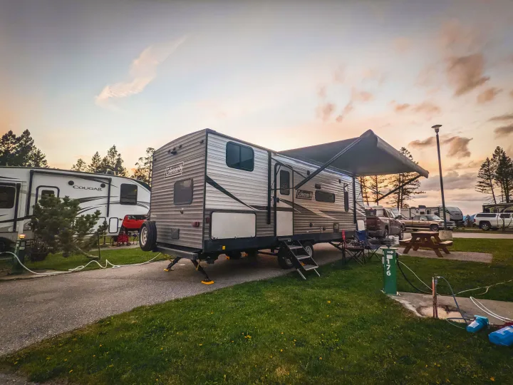 An RV rental, a Coleman travel trailer, parked at a spacious campsite with its awning extended under a colorful sky.. Coleman Lantern 2021
