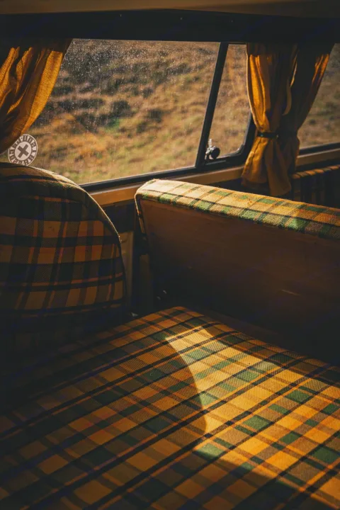 Cozy RV rental interior: warm sunlight illuminates green & yellow plaid seats, with a view of a field outside.. Volkswagen T2 Westfalia 1976