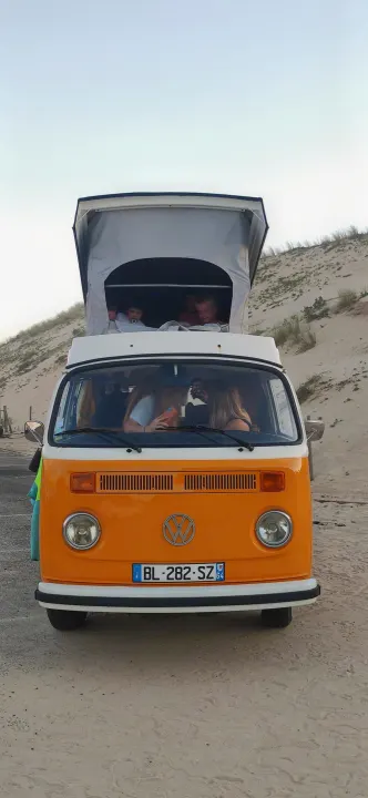 Iconic orange VW camper van RV rental with pop-top extended, kids and adults inside, parked on sandy dunes.. Volkswagen T2 Westfalia 1979