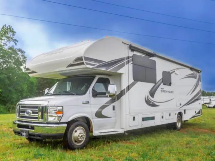 A white Jayco Greyhawk Class C RV, an excellent rv rental option, parked on a grassy field under a blue sky.. Jayco Greyhawk 2021