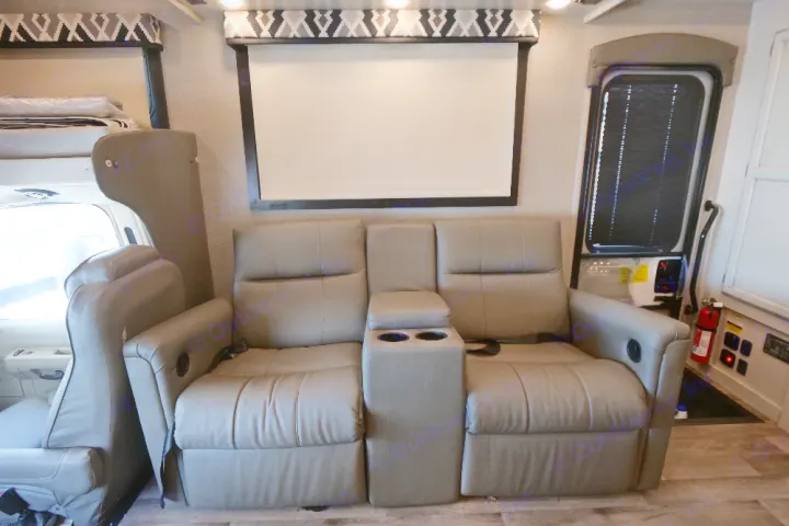 Relaxing RV rental interior featuring a grey leather reclining sofa with cup holders, large window, and cozy bunk area.. Jayco Greyhawk 2021