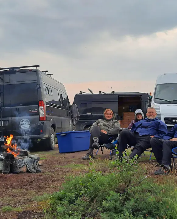 Friends enjoy a campfire evening with their RV rental vans. Boots dry by the fire, hinting at outdoor adventures & camping.. Dodge Promaster 2500 (Class B) 2022