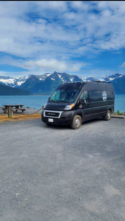 Black Ram ProMaster rv rental van parked by Alaskan water & snow-capped mountains. Ready for scenic outdoor adventures.. Dodge Ram 2500 (Class B) 2021