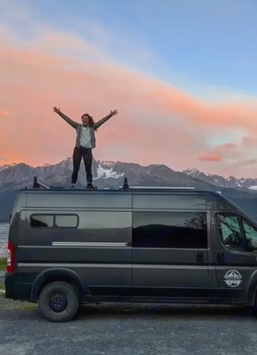 Joyful traveler on an RV rental van with arms outstretched, admiring the scenic mountain and sunset backdrop.. Dodge Ram 2500 (Class B) 2021