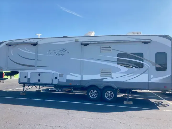 Large gray Open Range fifth-wheel RV rental, parked on asphalt under a blue sky, featuring multiple windows and two axles.. Open Range RV Open Range RV Fifth Wheel 2013