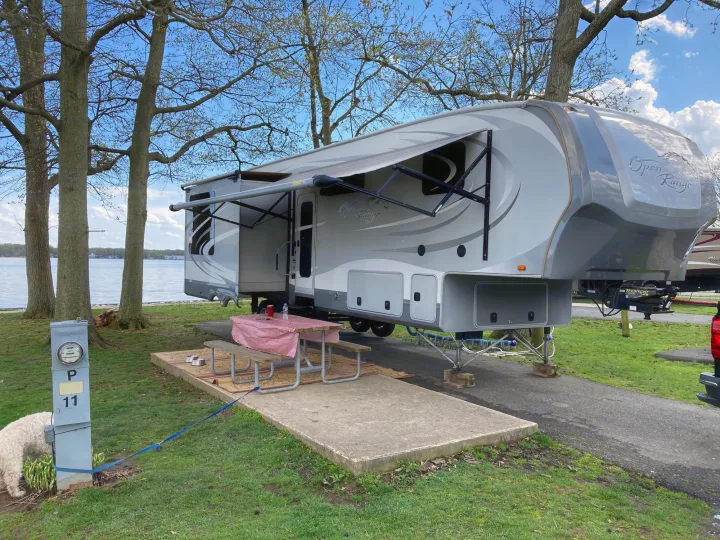 An RV rental parked at a picturesque lakeside campsite (P11) with an awning, picnic table, and a dog exploring.. Open Range RV Open Range RV Fifth Wheel 2013