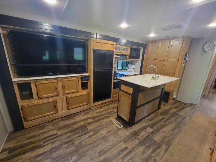Modern RV rental interior with a functional kitchen island, full-sized fridge, stove, and living area with TV.. Coachmen Freedom Express 323bhds 2019